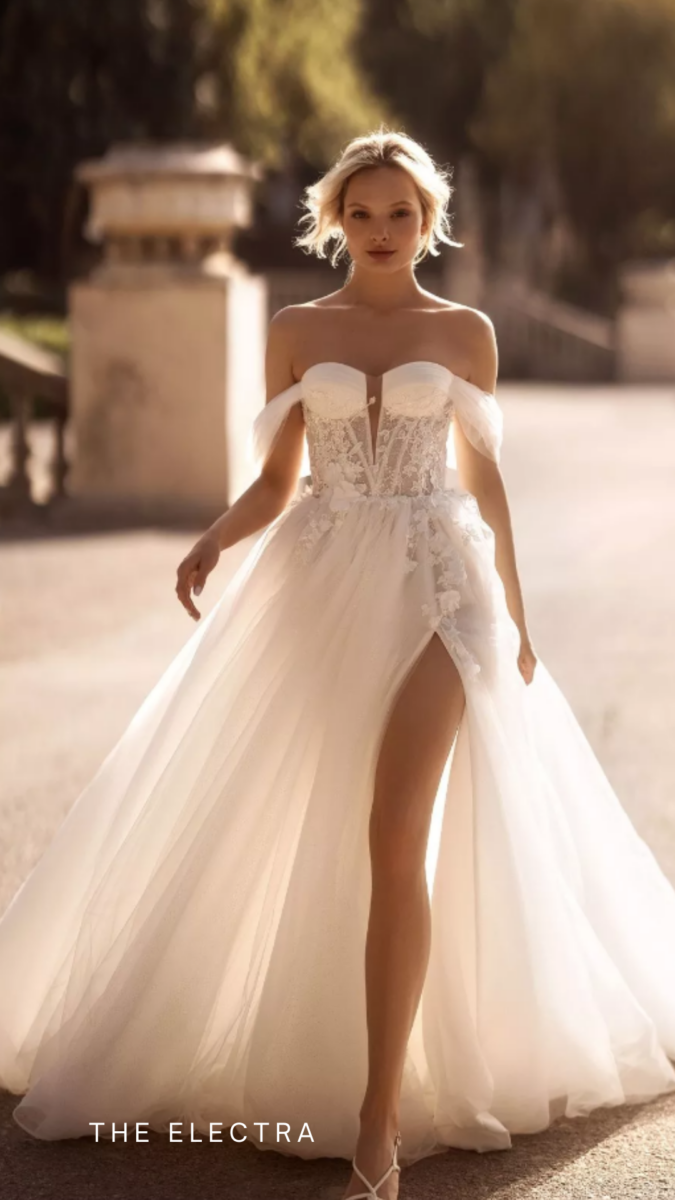 Woman in a white wedding dress with a high slit standing outdoors.